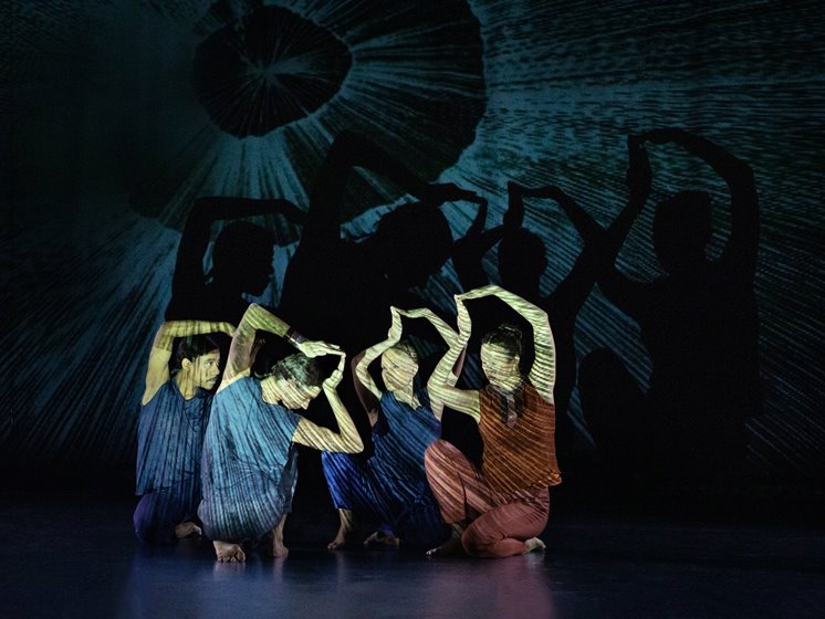 Fyra dansare sitter på huk med armarna ovanför huvudet.