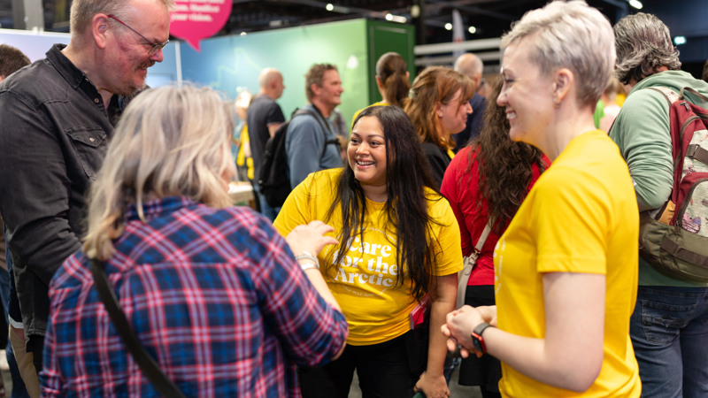 Två kvinnor i gula t-shirts  pratar med en man och en kvinna som besöker Move to Arctic Sweden, många människor i bakgrunden.