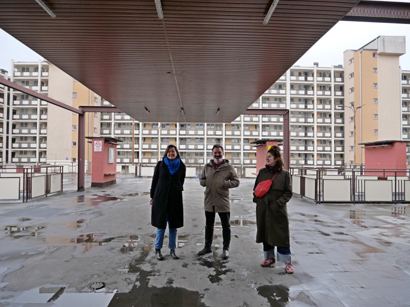 Tre personer står i ett bostadsområde med stora hyreshus.