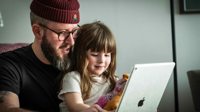 En man sitter med ett barn i famnen framför en dator