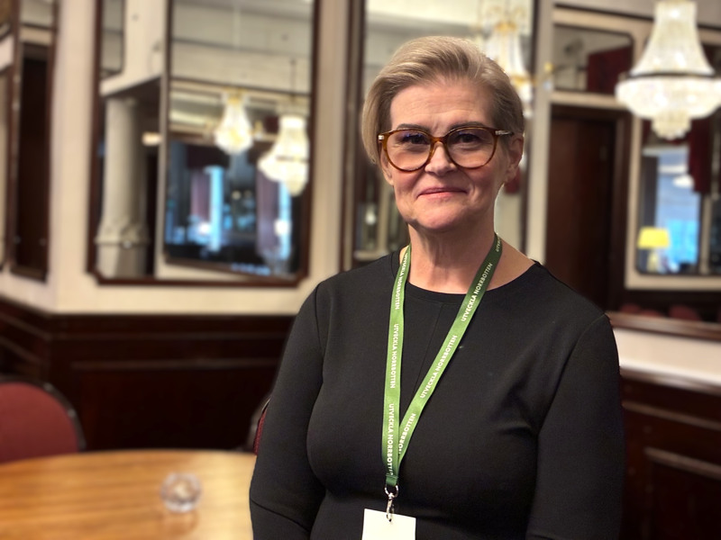 Ljushårig kortklippt kvinna med markerade glasögon i konferensmiljö.