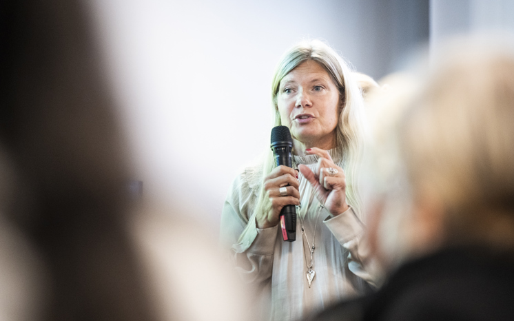 Kvinna talar i mikrofon framför publik.