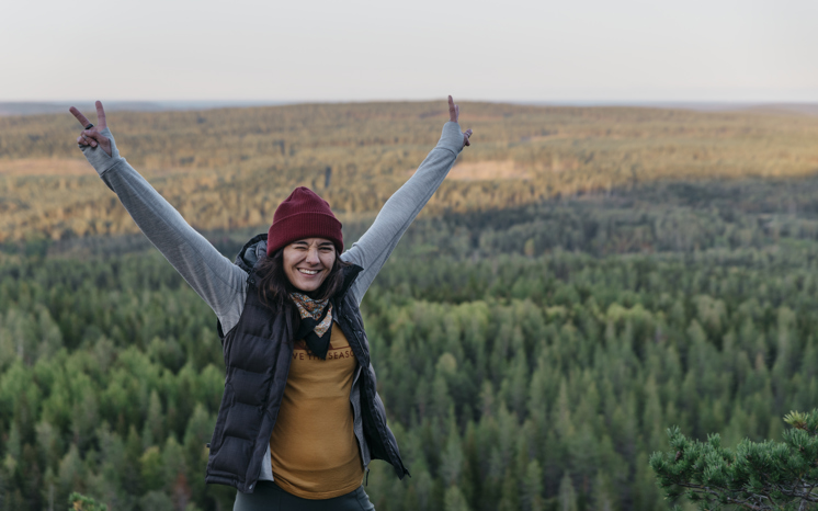 Leende kvinna med lyfta armar i skogslandskap
