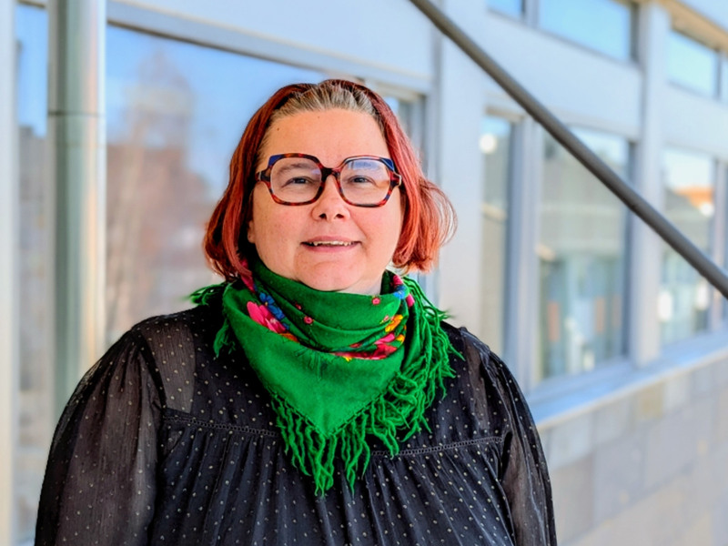 En kvinna med glasögon och en grön scarf.