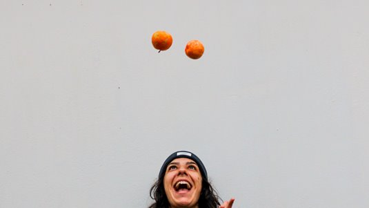 Glad kvinna i stickad tröja jonglerar med apelsiner.