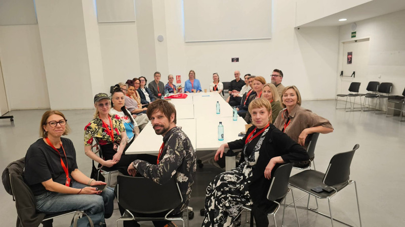 Människor runt ett konferensbord i ett vitt, kalt rum.