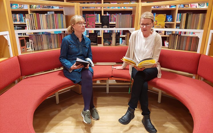 Två kvinnor läser i en soffa på ett bibliotek.