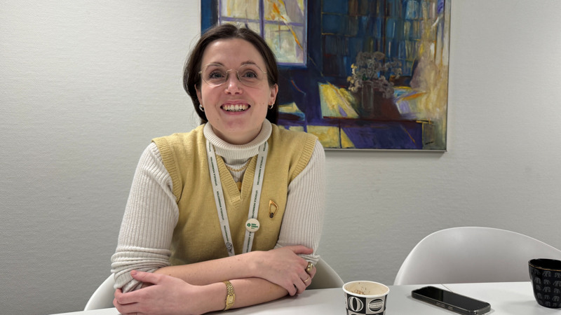 Carolina Lundmark Weinz sitter vid ett bord, i bakgrunden en målning.