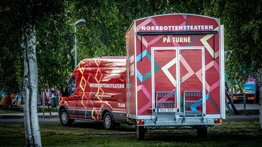 Norrbottensteaterns dekorerade fordon och släpvagn parkerad på gräsmatta.