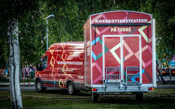 Norrbottensteaterns dekorerade fordon och släpvagn parkerad på gräsmatta.