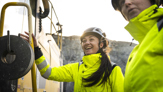 Två kvinnor i varselkläder och skyddshjälm pratar och skrattar.