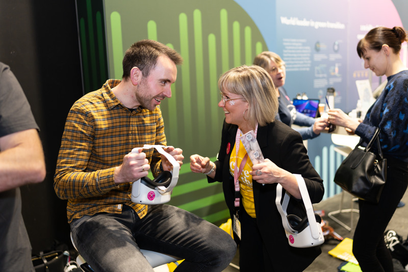 Sofi Wiippa Lahti, som representerar Överkalix, hjälper en mässbesökare med VR-glasögon.