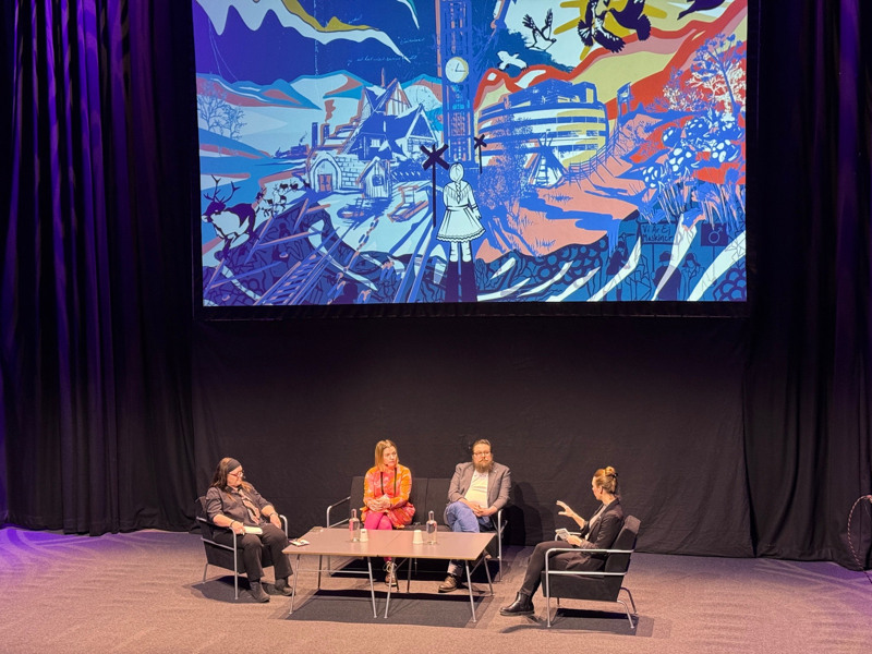 Fyra talare på scen under en skärm som visar en grafisk bild av Kiruna.