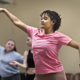 En ung tjej i rosa tröja sträcker på armarna i ett danssteg och två andra dansar i bakgrunden