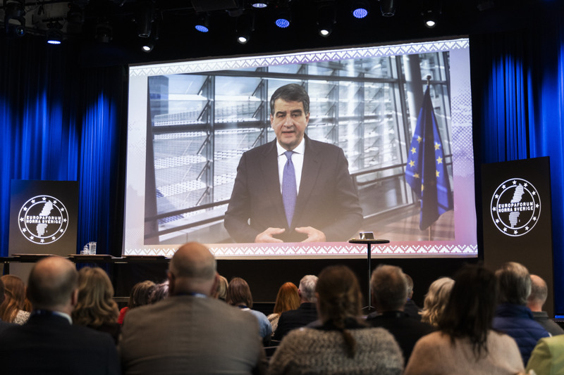 En video med EU-kommissionens vice ordförande Raffaele Fitto visas på en skärm på scenen, publik tittar på.