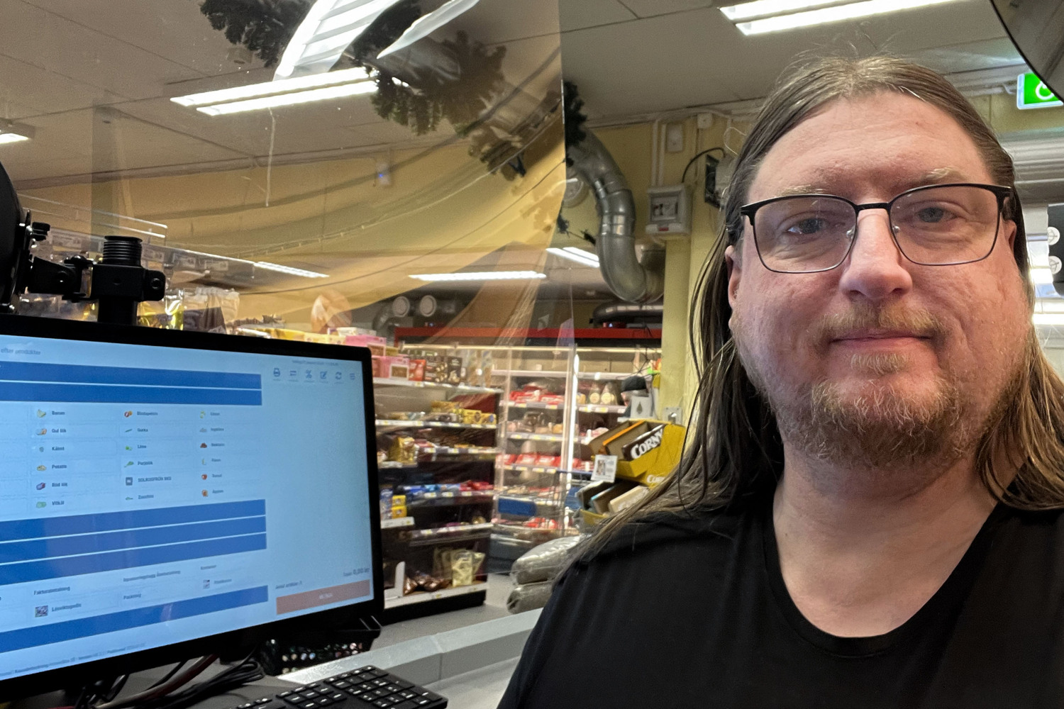 En man står framför en digital kassaskärm i butik.