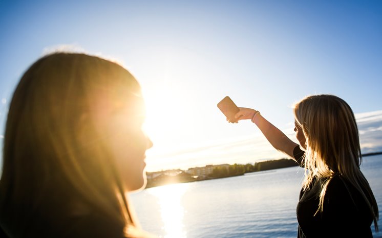 Två tjejer tar en selfie i motljus vid vatten.