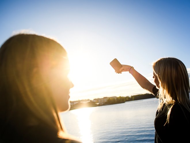 Två tjejer tar en selfie i motljus vid vatten.