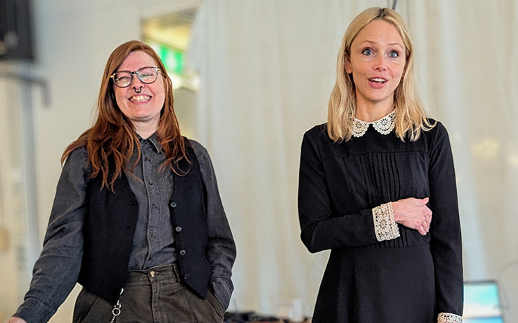 En skrattande mörkhårig kvinna och en ljushårig kvinna står och pratar på scen.