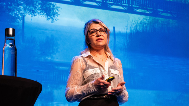 Mia Wahlström på scen under Kulturkraft, visar foto av ett vattendrag och en bro på skärmen bakom sig.