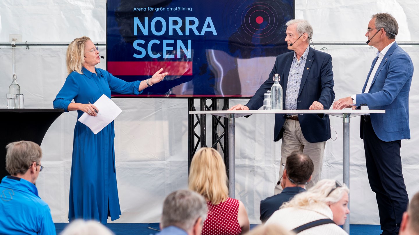 En kvinnlig moderator samtalar med två män på scen.