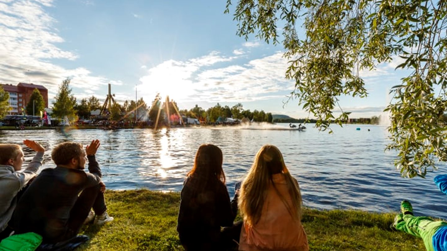 Människor sitter i gräset och ser ut över vatten.