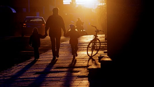 Vuxen med två barn promenerar i kvällssol. Foto: Susanne Lindholm.