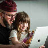 En man med en flicka i famnen sitter framför en bärbar dator.