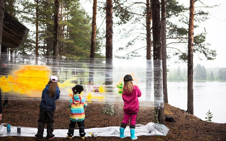 Barn målar på en genomskinlig plastfilm uppställd mellan träd.