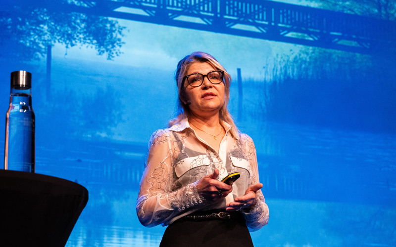 Mia Wahlström på scen under Kulturkraft, visar foto av ett vattendrag och en bro på skärmen bakom sig.