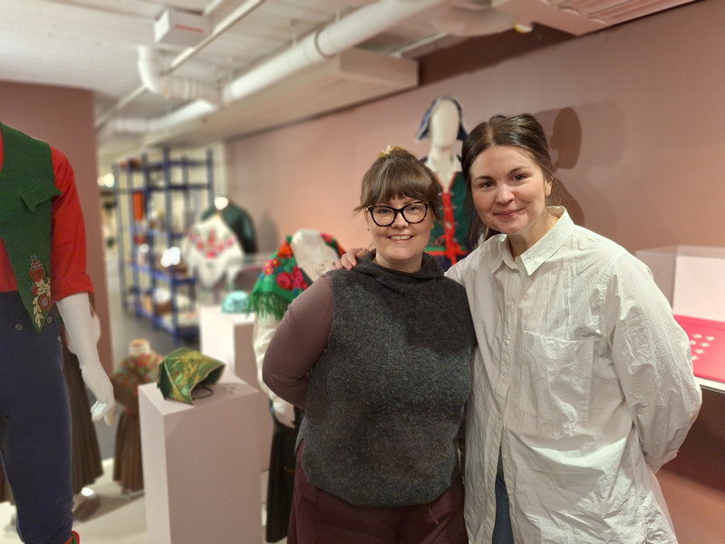 Sofia Öberg och Linnea Nilsson i utställningslokalen med folkdräkter i bakgrunden.