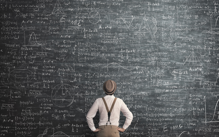 Ryggtavlan av en man som står framför en stor griffeltavla och försöker lösa ett matematiskt problem.