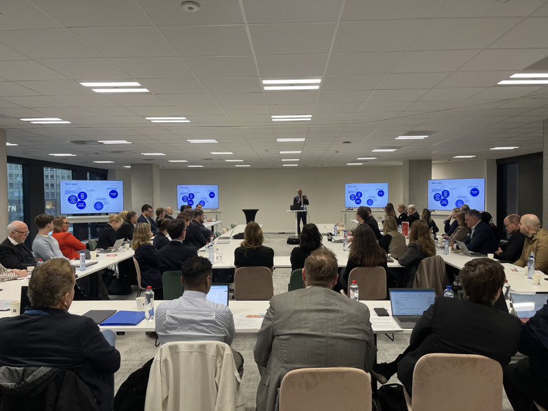 Ryggarna av ett 60-tal personer som tar del av en presentation.