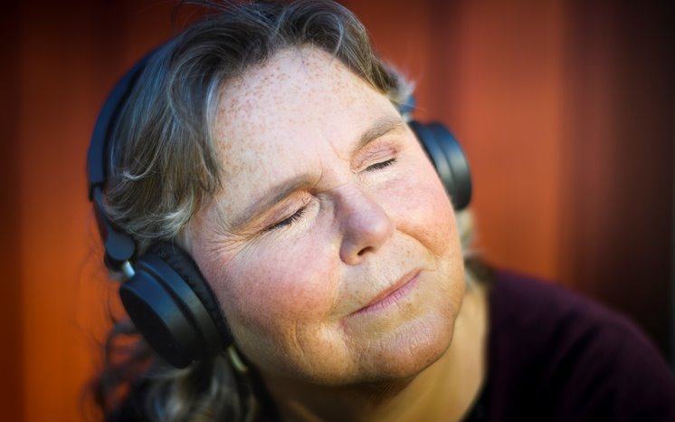 Äldre kvinna med hörlurar lyssnar njutningsfullt.