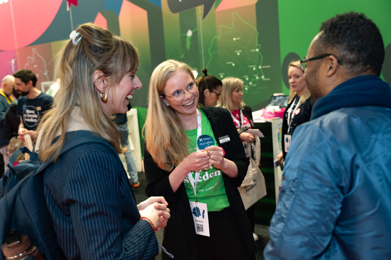 Marcella de Geus pratar med en manlig och en kvinnlig mässbesökare, de skrattar.