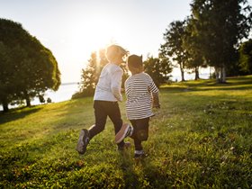 Två barn springer på gräsmatta i solnedgång