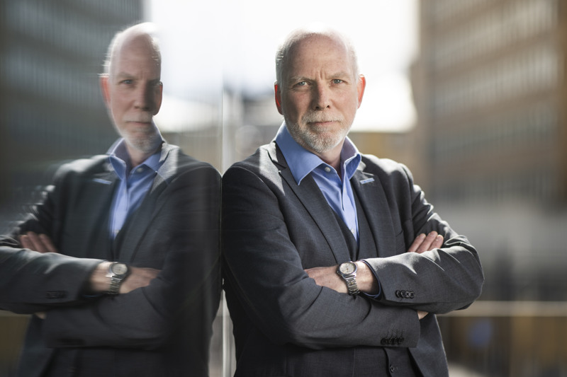 Amders Öberg står lutad mot ett fönster med armarna i kors, hans reflektion syns i fönstret.