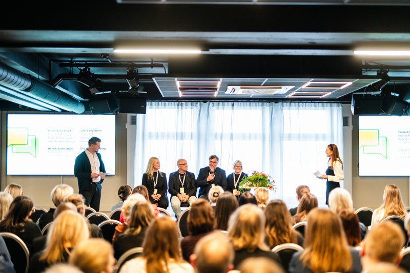 Fyra personer i en panel intervjuas inför publik av två moderatorer.