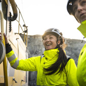 Två kvinnor i skyddskläder och skyddshjälm står vid ett gruvfordon i ett gruvschakt