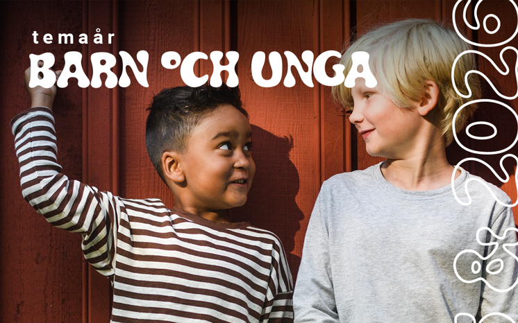 Två glada pojkar lutar sig mot en röd trävägg.