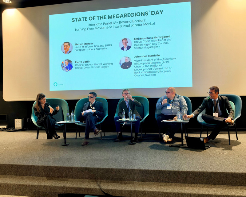 Fem talare sitter på en scen framför en skärm där det står State of the Megaregions day.