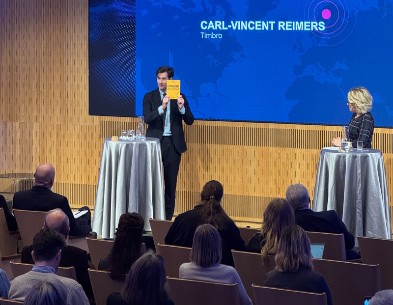 Carl-Vincent Reimers, Timbro, håller upp en rapport på scenen, publik i förgrunden.